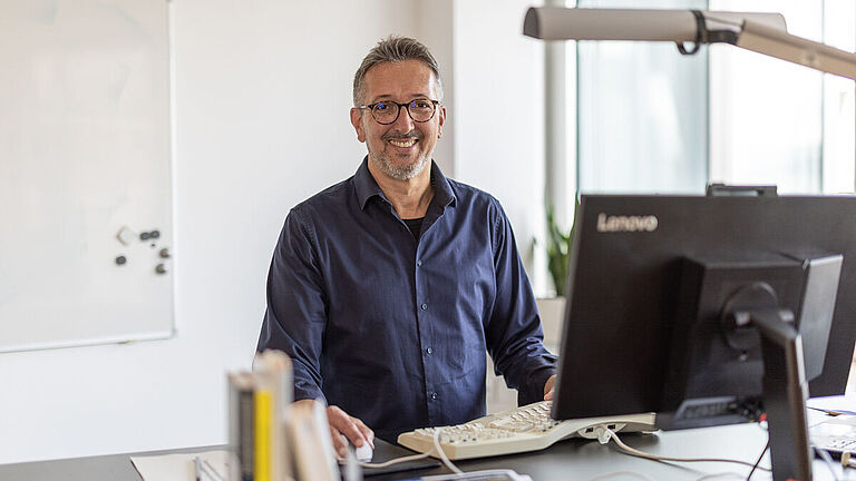 Karl-Josef Thielen am Schreibtisch vor PC, lächelt in Kamera 