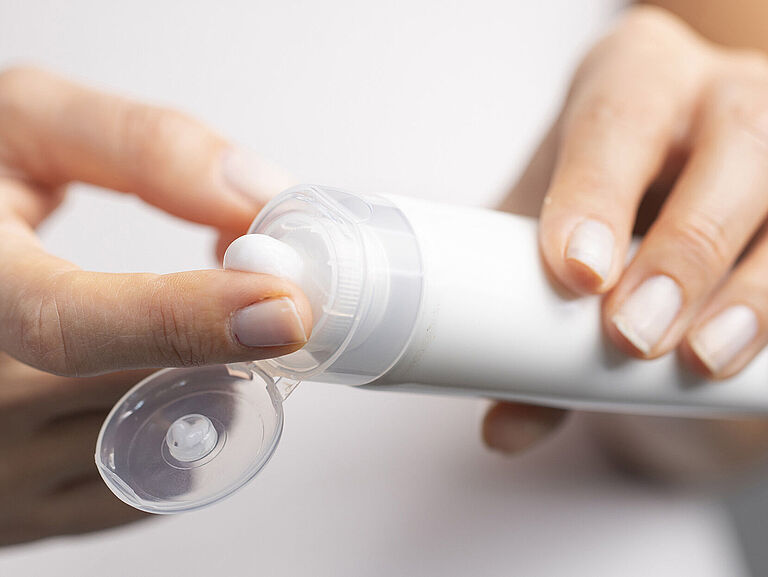 Weibliche Hände. Rechte Hand entnimmt Handcreme aus einer weißen Tube.