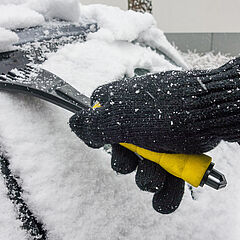 Nahaufnahme eines Eiskratzers an verschneiter Autoscheibe