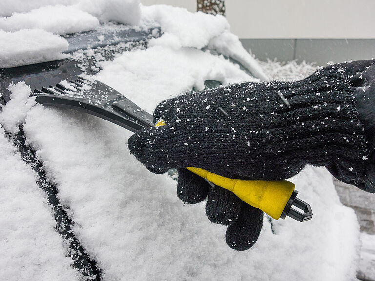 Nahaufnahme eines Eiskratzers an verschneiter Autoscheibe