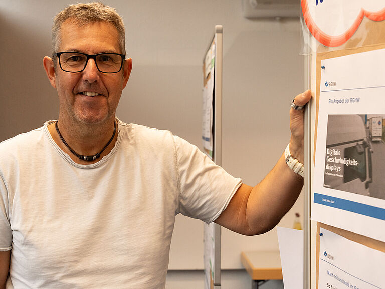 Simon Mewes, ein Seminarteilnehmer mit kurzen grauen Haaren, Brille und im weißen T-Shirt, steht am Flipchart und schaut freundlich in die Kamera. 