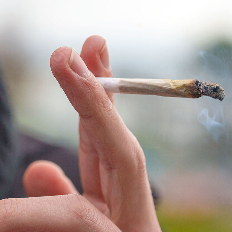 Das Bild zeigt eine Hand, die einen brennenden Joint hält. Das Bild wurde bei der Studie Cannabis und Autofahren aufgenommen.