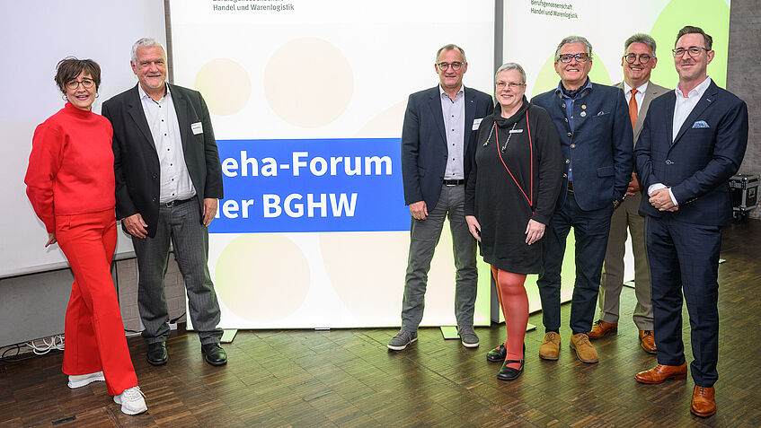 Gruppenbild: Mitglieder der BGHW- Selbstverwaltung, Geschäftsführung und Führungskräften stellten sich zu einem Foto zusammen. Links vom leuchtenden Logo Reha-Forum: Marita Klinkert, Manfred Wirsch und rechts davon (von links): Roland Kraemer Gabriele Menge-Ullbrich, Dr. Udo Schöpf, Martin Kögler, Sven Königer 