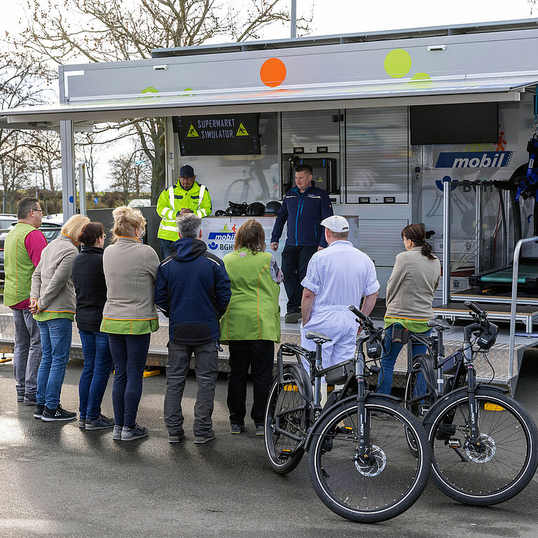 Mehrere Personen stehen mit dem Rücken zur Kamera. Sie hören den Trainern des BGHW-mobil zu, die zum Thema Sicherheit informieren. 