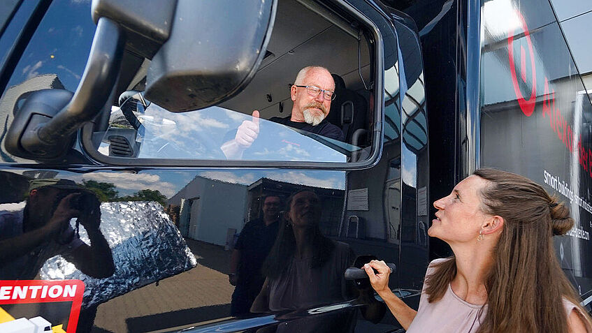 Eine Frau steht an der Fahrertür eines Lkws und spricht mit dem Fahrer durch das geöffnete Fenster