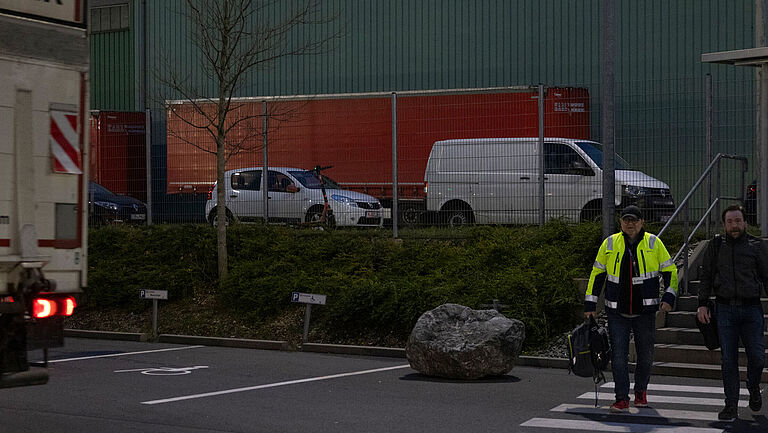 DB Schenker in Nürnber, ein dunkel gekleideter Mitarbeiter und ein Mitarbeiter mit Warnschutzjacke kommen im Dunkeln auf das Betriebsgelände.