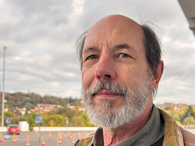 Professor Wolfgang Fastenmeier blickt freundlich in die Kamera. Im Hintergrund sieht man den Parcours für die Fahrübungen der Probenden.