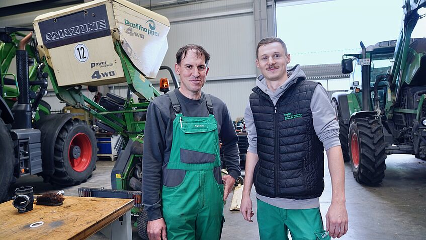 Zwei Männer in Arbeitskleidung in einer Werkshalle.
