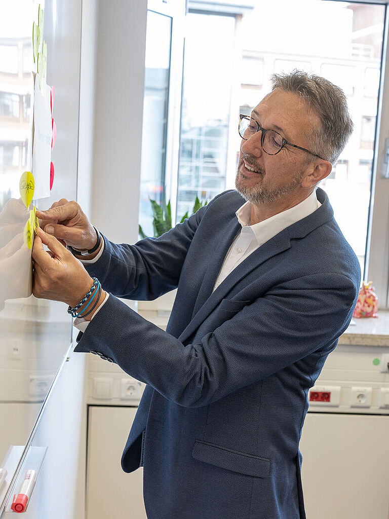 Karl-Josef Thielen mit blauem Sakko, klebt Post-Its an an eine Tafel.