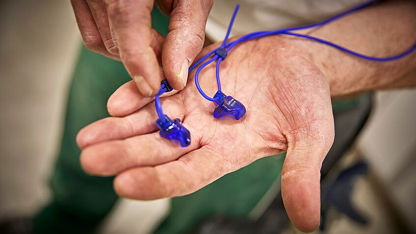 Auf einer Hand liegt eine blaue Otoplastik, ein individuell angefertigter Gehörschutz