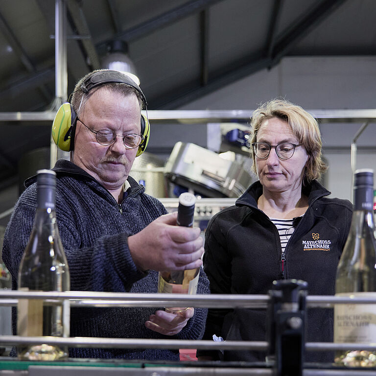 Astrid Rickert (rechts) und Günter Schumacher schauen sich die Weinflaschen an, die auf einem Band vor ihnen die Abfüllanlage durchlaufen. 