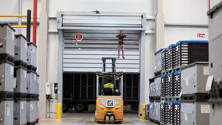 Das Bild zeigt einen Gabelstapler vor einem Tor, das sich öffnet.