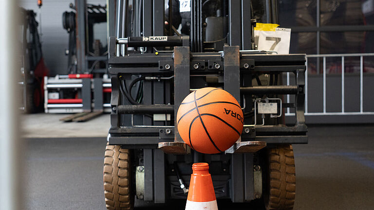 Ein orangefarbener Basketball wird auf auf der Zinke eines Gabelstaplers geführt. 