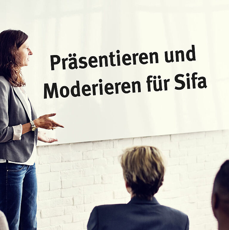 Eine Frau steht vor einer Präsentationstafel mit der Aufschrift: Präsentieren und Moderieren für Sifa. Seminarteilnehmende sitzen davor und hören zu.