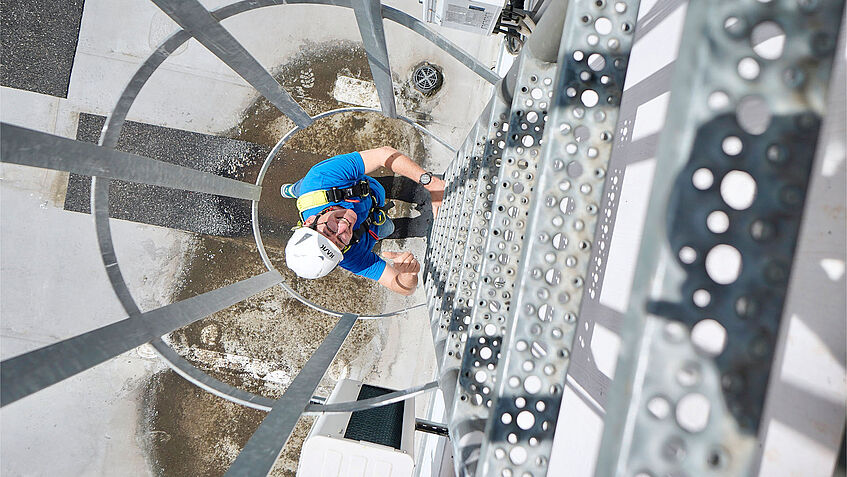 Eine Haustechniker klettert eine Leiter mit Rückfallschutz hoch.