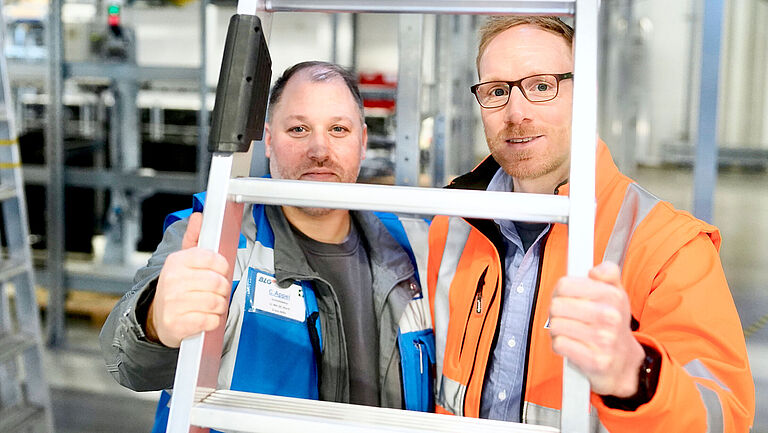 Schichtleiter Christian Appel und Thomas Menke, Leiter Operations Kommissionierung, schauen durch eine Leiter.