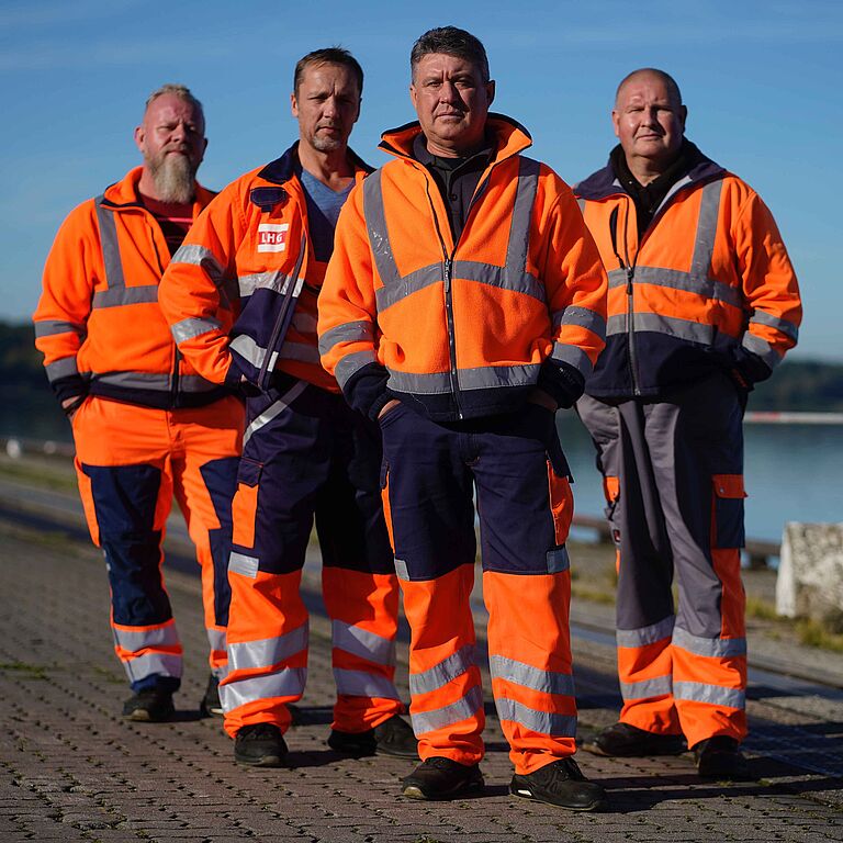 Vier Hafenmitarbeiter in Arbeitskleidung stehen im Hafen.