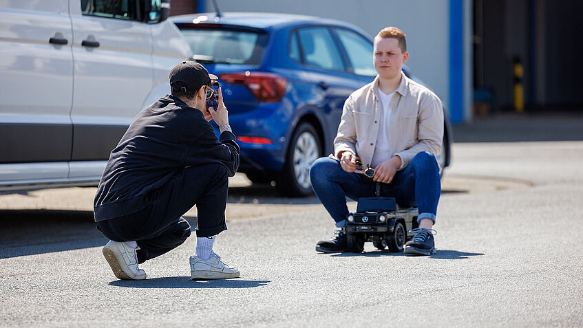 Ein junger Mann auf einem Bobbycar wird von einem anderen gefilmt