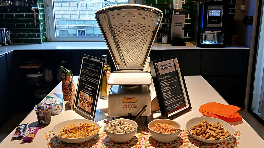 Tisch auf dem eine große Lebensmittelwaage steht, darum herum stehen Schüsselchen mit Lebensmitteln