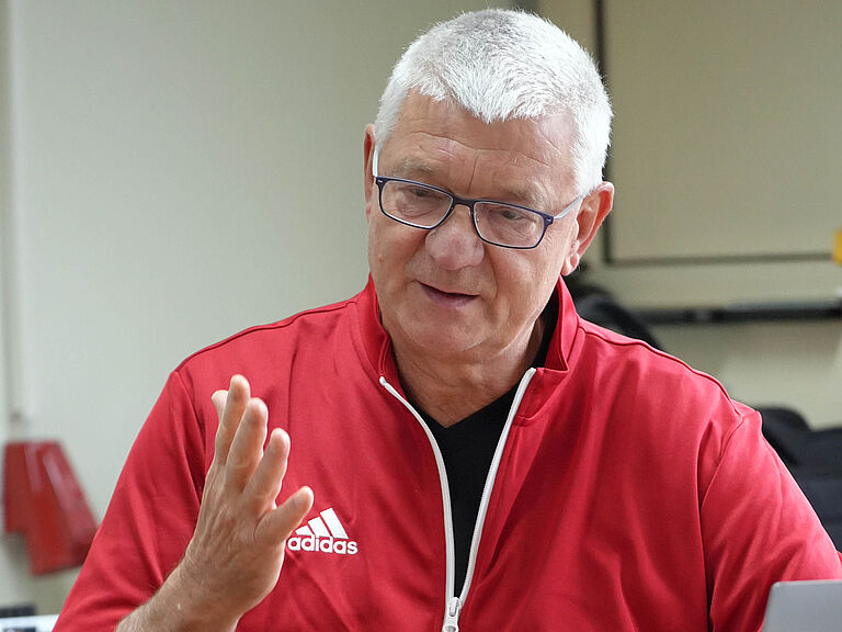 Peter Richarz, ein Sportcoach und Trainer, sitzt an einem Tisch und spricht gestikulierend. 