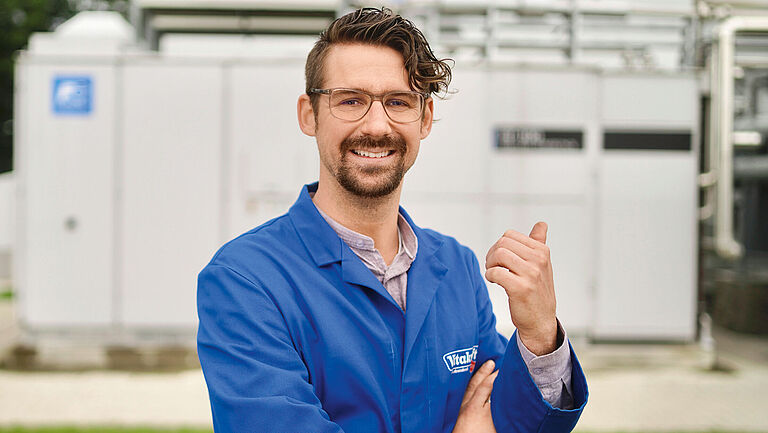 Dennis Schwega, technischer Leiter bei Vitakraft, steht vor der Brennstoffzellenanlage und hebt seinen linken Daumen.