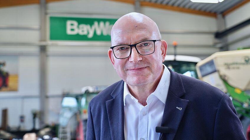 Ein Mann im Jacket steht in einer Werkshalle.