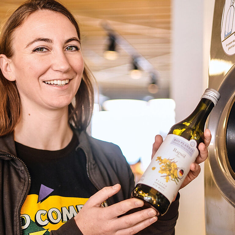 Anne Schill, Fachbereichsleiterin Trockensortiment, mit einer Mehrwegölflasche am Pfandautomaten.
