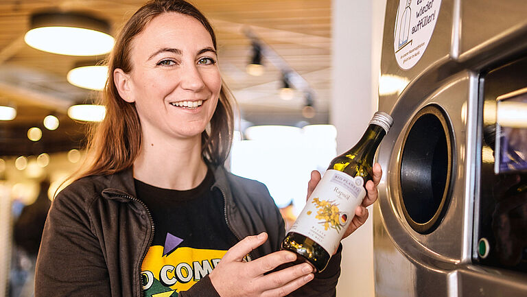 Anne Schill, Fachbereichsleiterin Trockensortiment, mit einer Mehrwegölflasche am Pfandautomaten.