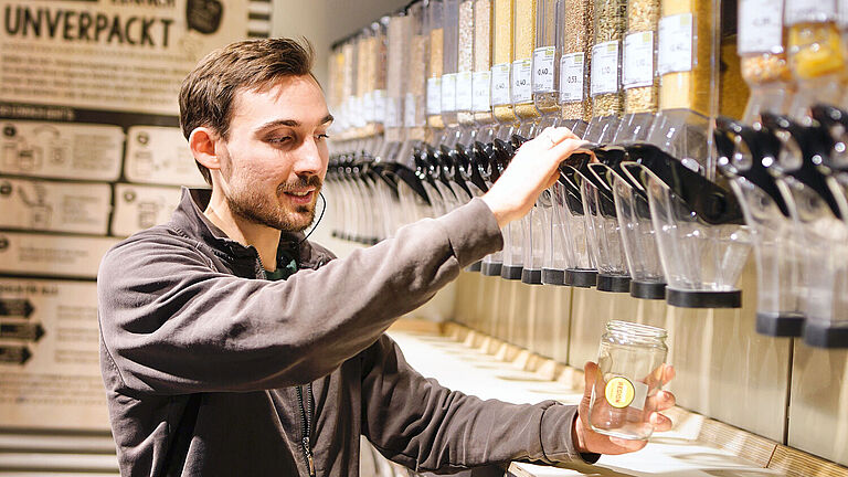 Abteilungsleiter Florian Maertz füllt an der Unverpackt-Station Ware in ein Mehrwegglas.