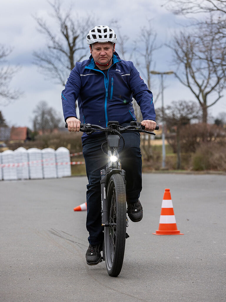 BGHW-Trainer Sven Krämer fährt mit dem E-Bike auf die Kamera zu. Er trägt einen Fahrradhelm. Er zeigt, was beim E-Bike-Fahren zu beachten ist. 
