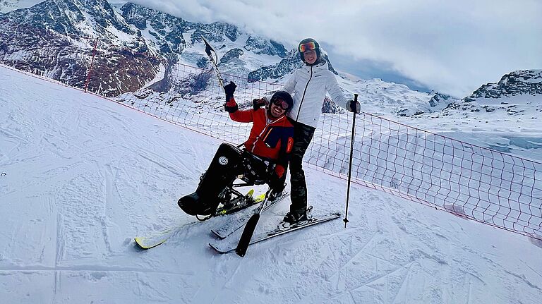 Der querschnittgelähmte Christoph Weis sitzt in einem Monoski, hinter ihm steht seine Lebensgefährtin auf Skiern. In einer verschneiten Berglandschaft lachen sie gemeinsam in die Kamera. 
