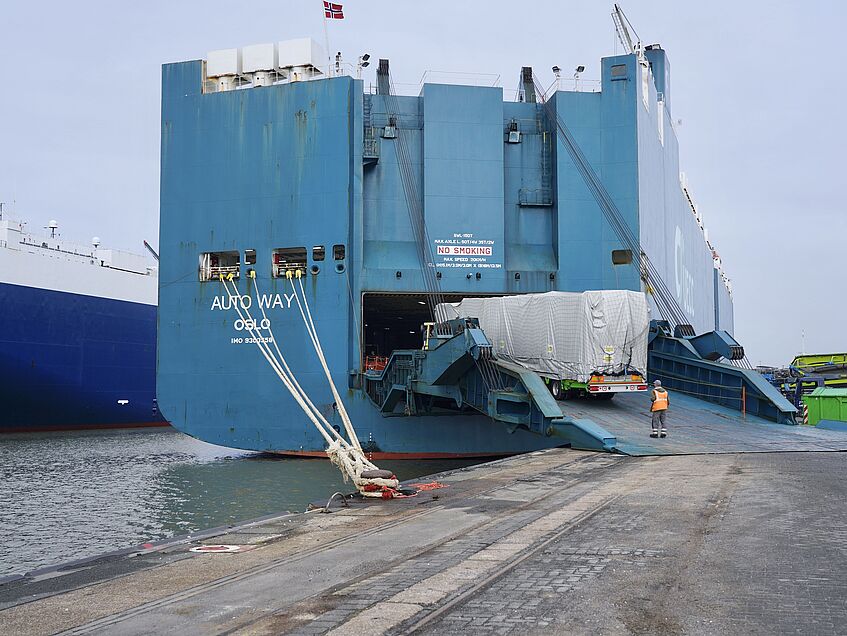 Autotransportschiff am Kai, Fahrzeug wird über Rampe verladen.
