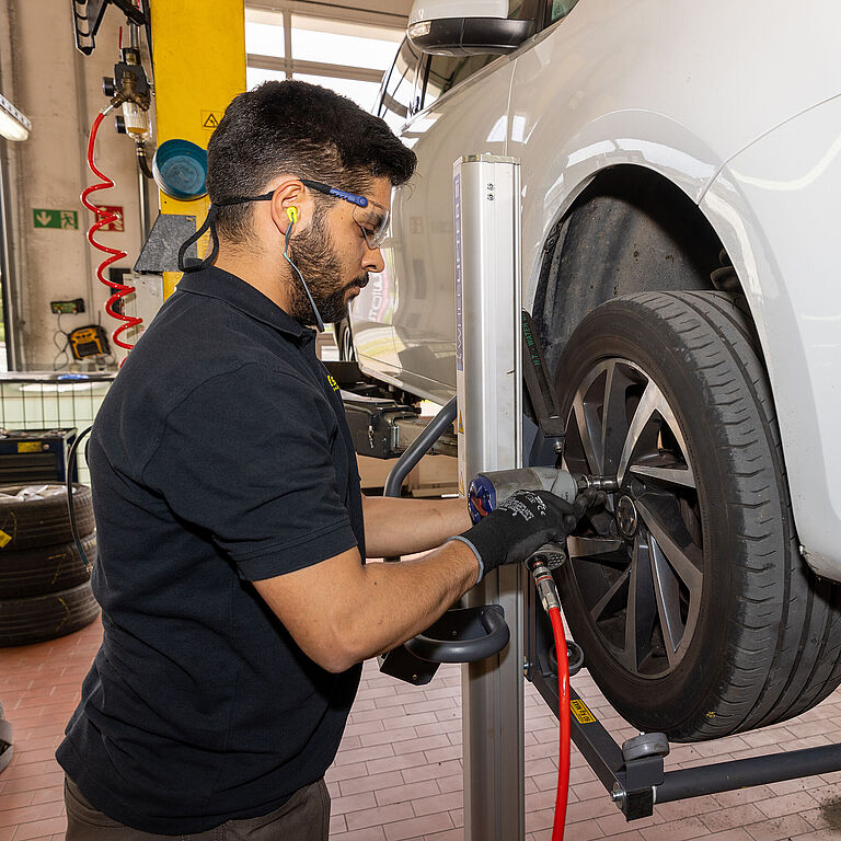 Ein Beschäftigter in einer Kfz-Werkstatt bei der Reifenmontage an einem Auto auf einer Hebebühne
