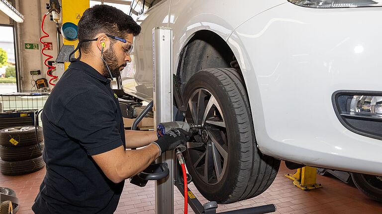 Ein Beschäftigter in einer Kfz-Werkstatt bei der Reifenmontage an einem Auto auf einer Hebebühne