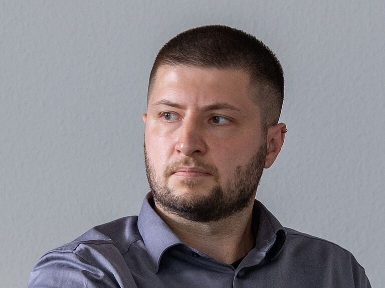 Lars Klose sitzt auf einem Stuhl und schaut mit ernstem Blick nach rechts. Er ist im Porträt zu sehen.