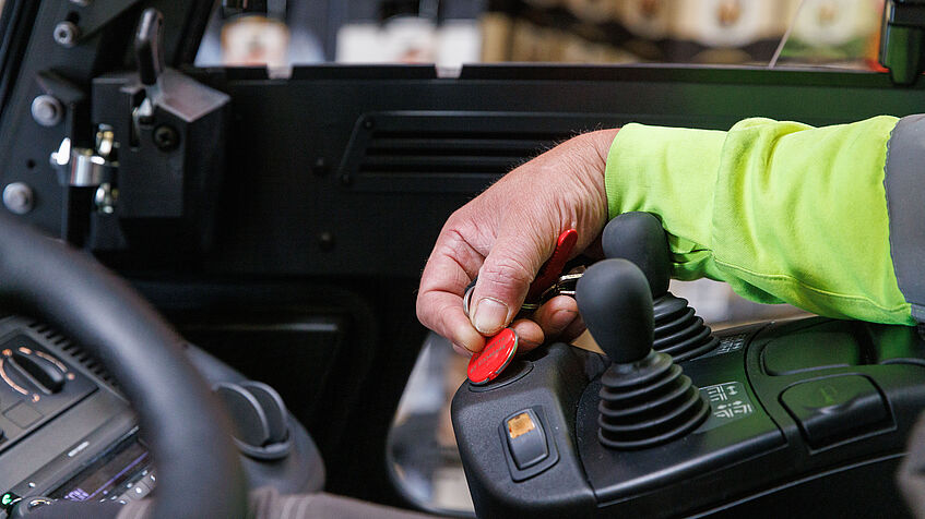 Das Bild zeigt das Fahrerhaus eines Gabelstaplers und die rechte Hand des Gabelstaplers Dirk Boßmer, der einen roten Chip an die Armaturen hält. Damit lässt sch der Stapler auf den Prothesenträger einstellen.
