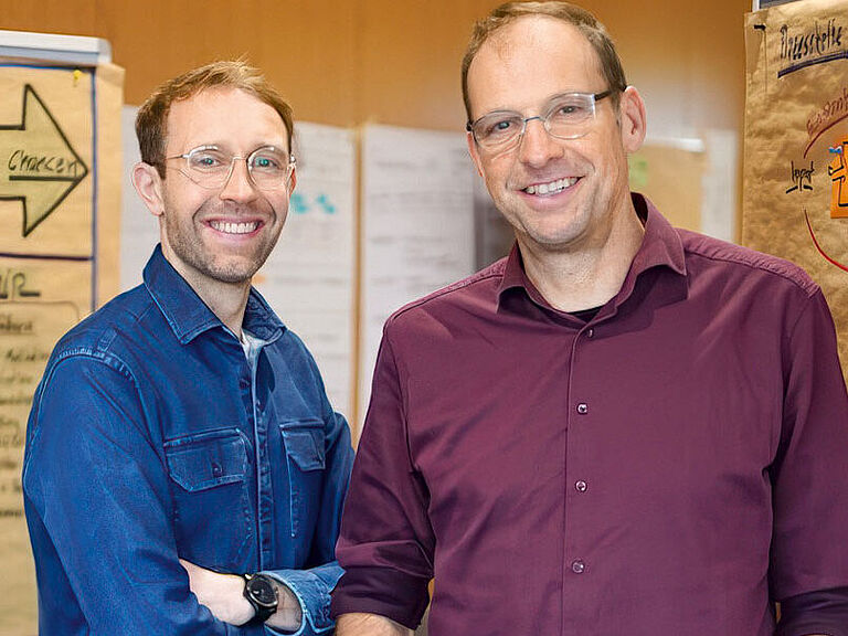 Zwei Personen stehen zwischen Moderationspinnwänden in einem Seminarraum