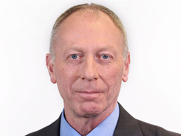 Porträt von Kay Schulte. Ein Mann mittleren Alters mit kurzen, hellen Haaren steht vor einem neutralen weißen Hintergrund. Er trägt einen dunkelgrauen Anzug, ein hellblaues Hemd und eine dunkelblaue Krawatte mit dezentem Punktmuster. Auf dem Revers seines Jacketts ist ein kleines DVR-Logo (Deutscher Verkehrssicherheitsrat) zu erkennen. Er blickt ruhig und freundlich in die Kamera.