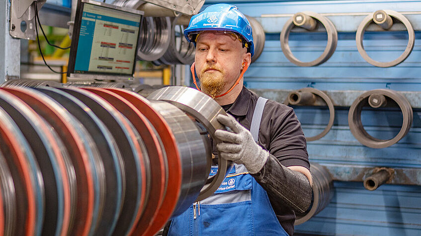 Ein Mitarbeiter mit Schutzhelm bestückt ein Stahlrohr mit Stahlringen.