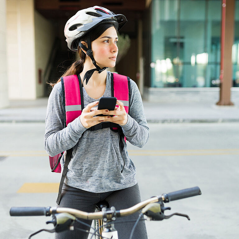 Eine junge Frau sitzt auf dem Fahrrad und hält ihr Smartphone in der Hand