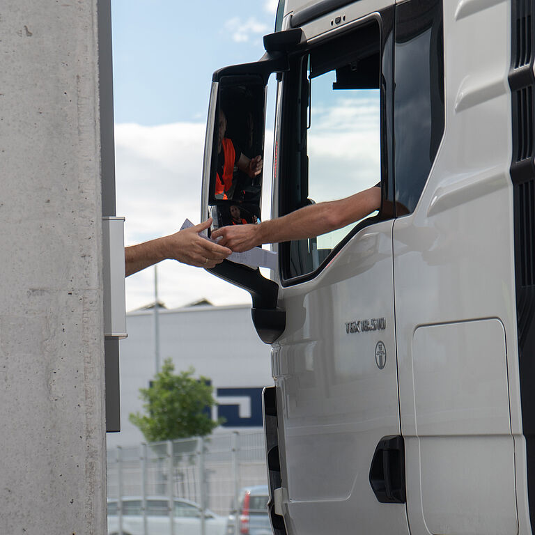 LKW-Fahrer überreicht L’ORÉAL-Mitarbeiter bei der Ausfahrt ein Dokument. 