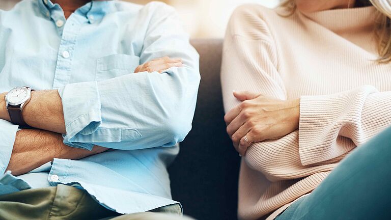 ein Mann und eine Frau sitzen mit verschränkten Armen nebeneinander auf einem Sofa