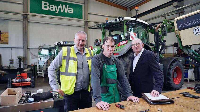 Drei Männer stehen in einer Werkshalle.