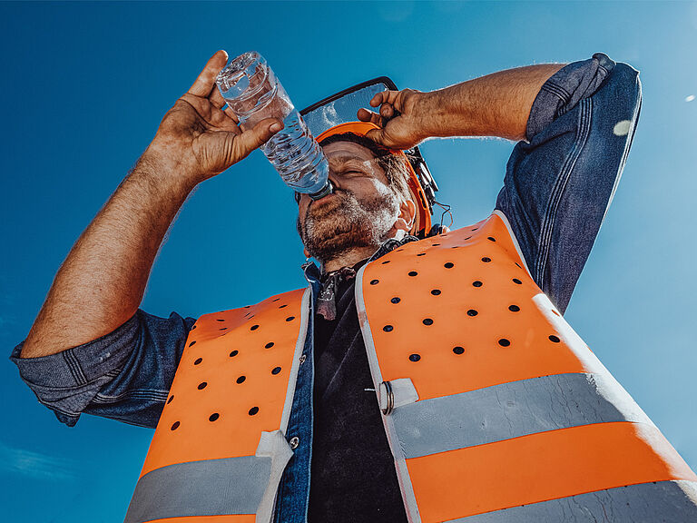 Arbeiter mit Warnweste trinkt bei Hitze an einer Flasche Wasser