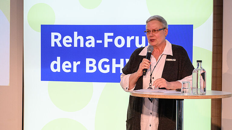 Gabriele Menge-Ullbrich, alternierende Vorsitzende des Klinik- und Reha-Ausschusses der BGHW-Selbstverwaltung, steht an einem Stehtisch auf der Bühne des BGHW-Reha-Forums und spricht in ein Mikrofon. 