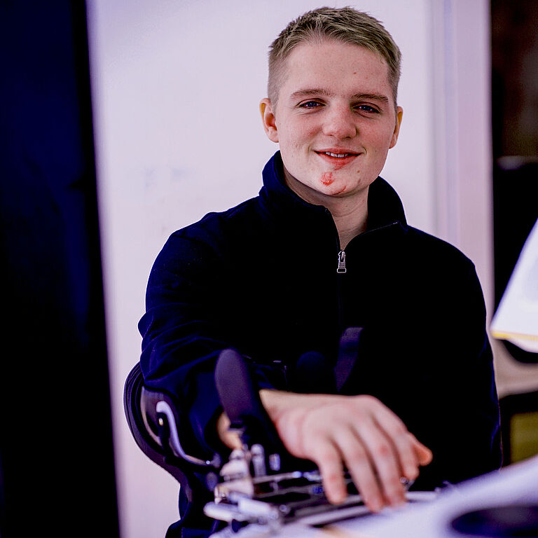 Porträtfoto von Lars Eberhard. Er trägt einen dunklen Pulli und schaut freundlich in die Kamera. Seine verletzte rechte Hand ist unscharf im Vordergrund zu sehen.