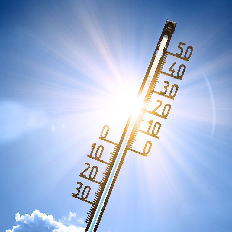 Ein Thermometer ragt in den sonnigen Himmel. Es zeigt 34 Grad Celsius an.