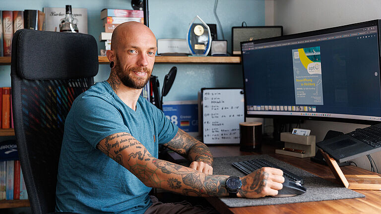 Kim Cremer sitzt im Sportdress an seinem Schreibtisch vor einem Computer-Bildschirm. Er arbeitet zeitweise im Homeoffice. 