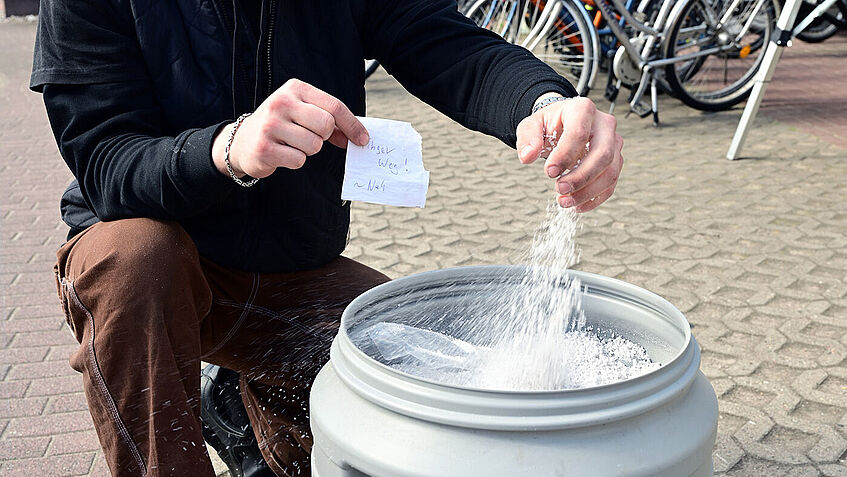 Junger Mann hockt hinter einem geöffneten Spezialbehälter mit Löschgranulat.