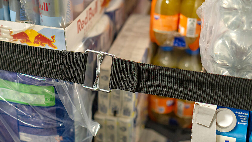 Ein Rollcontainer mit aufeinander gestapelten Waren wird mit einem Gummispanngurt zusammengehalten.